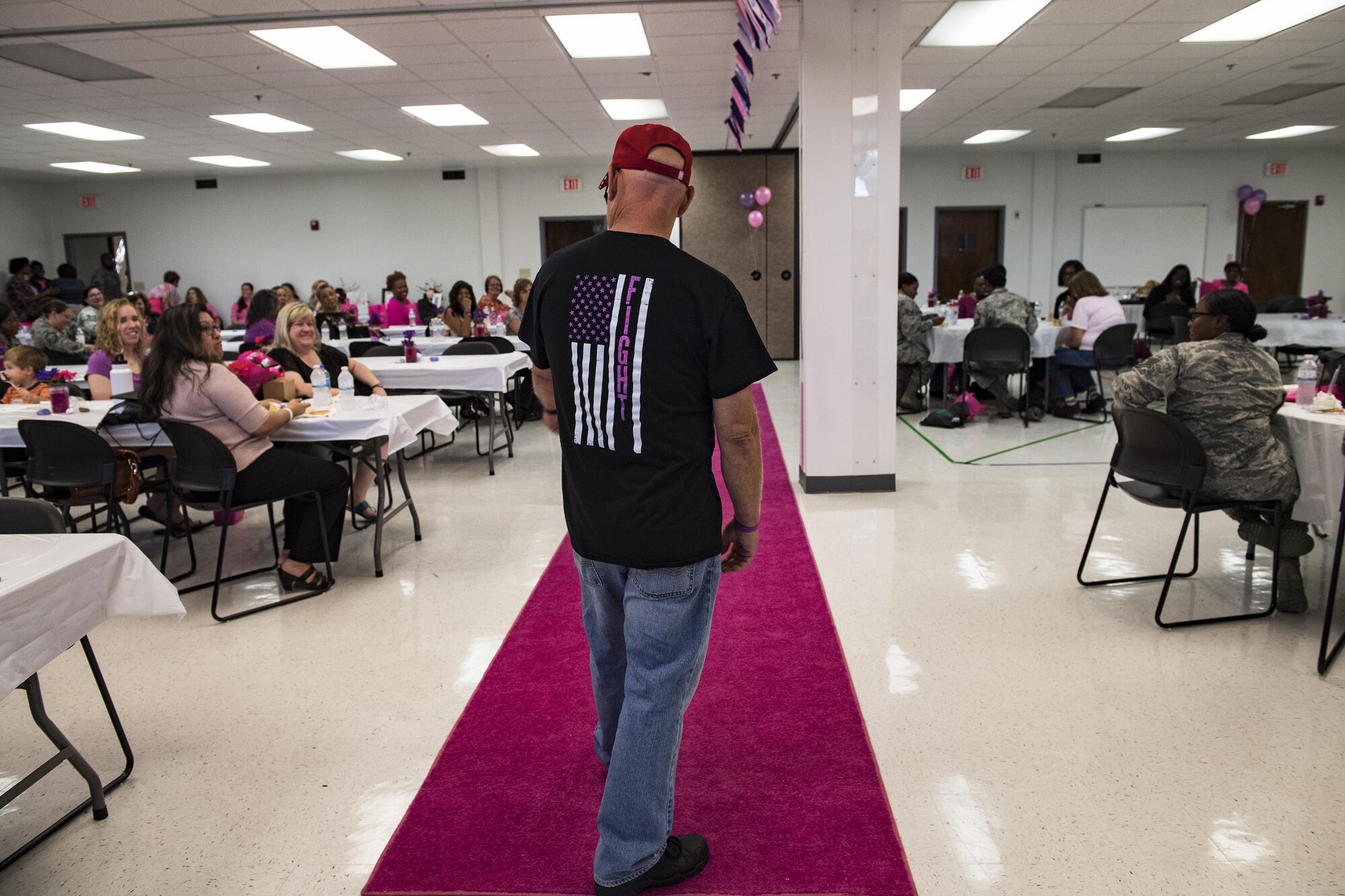 A volunteer poses on a pink runway while modeling during a Pink and Purple Luncheon, Oct. 19, 2017, at Moody Air Force Base, Ga. The luncheon was designed to raise awareness about breast cancer and encourage everyone to speak-up about domestic violence. To lighten the mood, commissary workers modeled clothing that raises awareness for both causes. (U.S. Air Force photo by Senior Airman Janiqua P. Robinson)