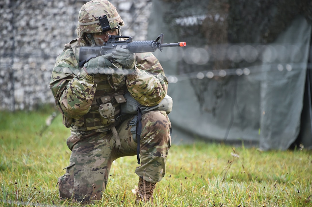 A kneeling soldier sights down a paintball rifle during training.