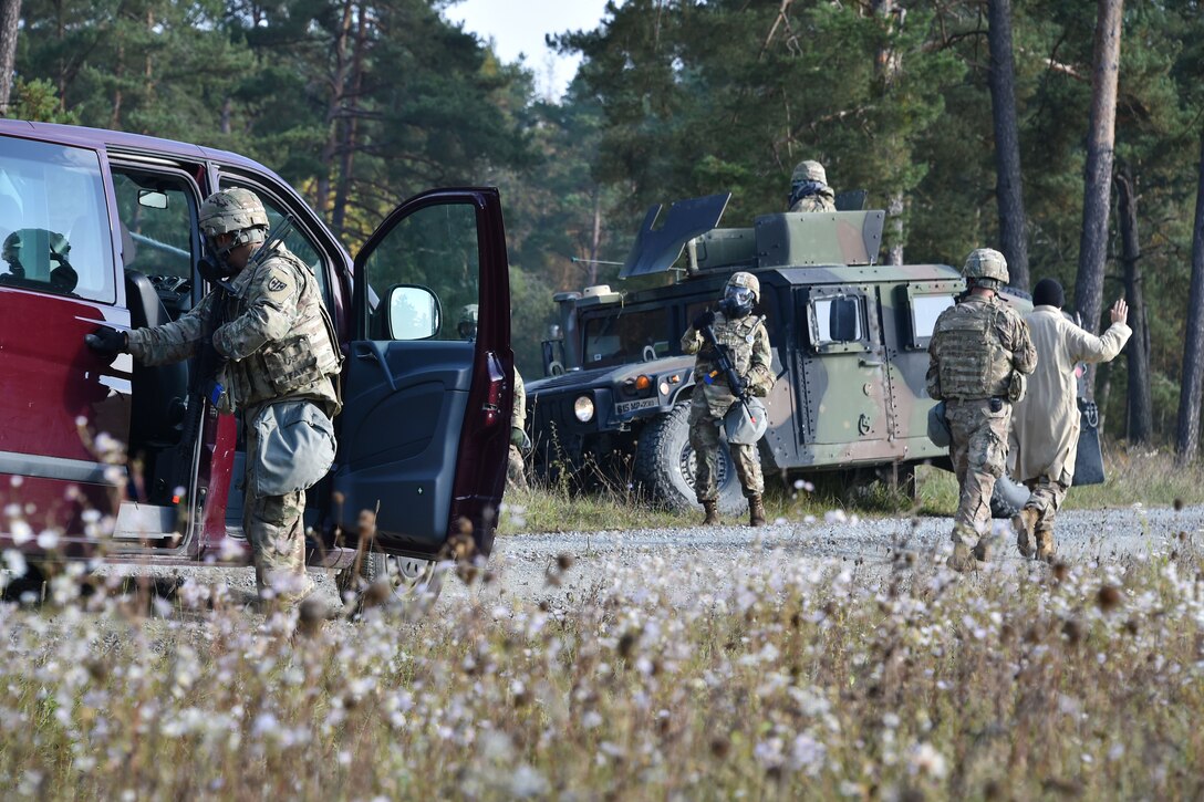A soldier searches a civilian vehicle while others provide security from a humvee.
