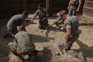 Men sit in the sand with containers.