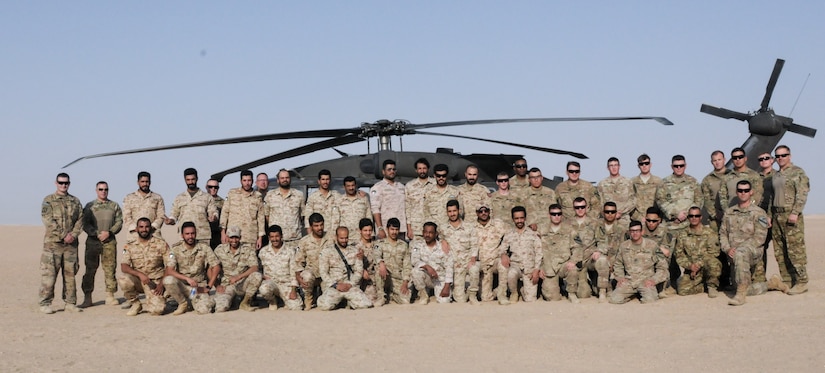 U.S. and Kuwaiti soldiers pose for a photo in front of a helicopter.