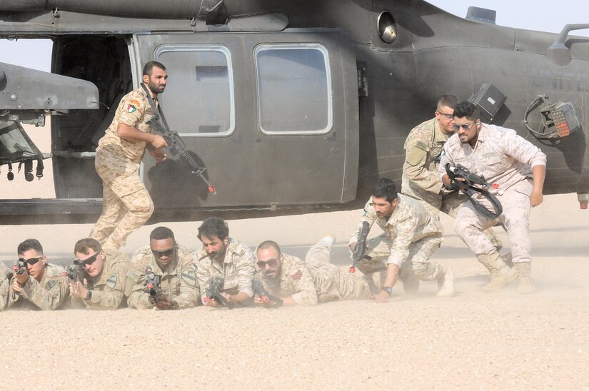 U.S. and Kuwaiti soldiers in position on the ground in front of a helicopter.