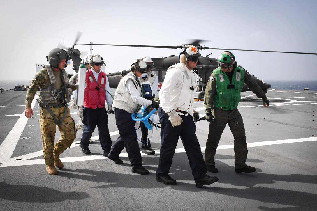 Sailors and soldiers transport a patient on a stretcher.