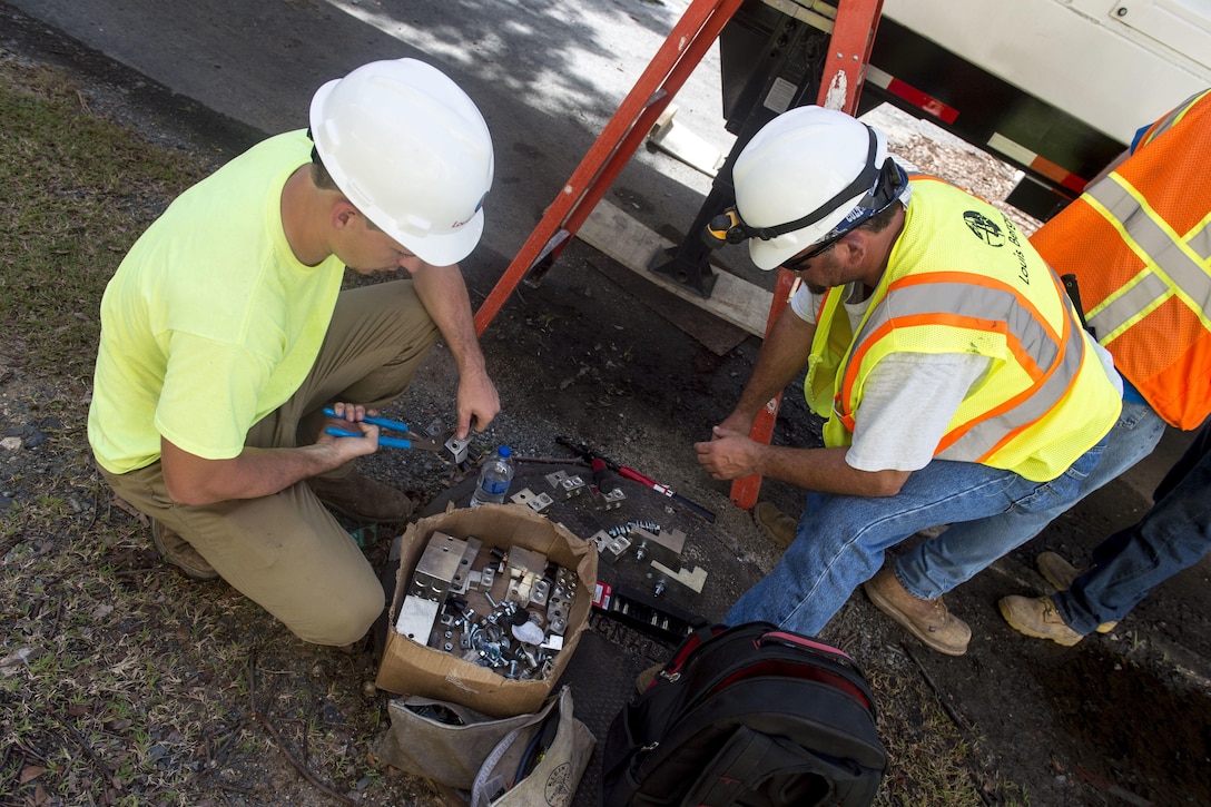 Men in protective gear prepare metal connectors for high voltage cables.