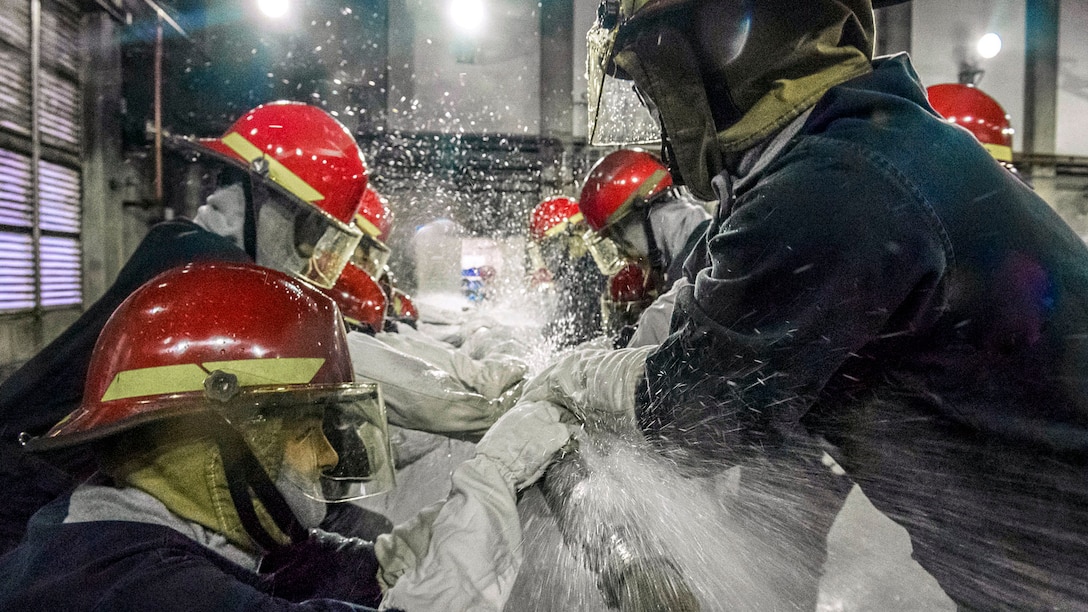 Sailors hold are near a pipe with water spraying.