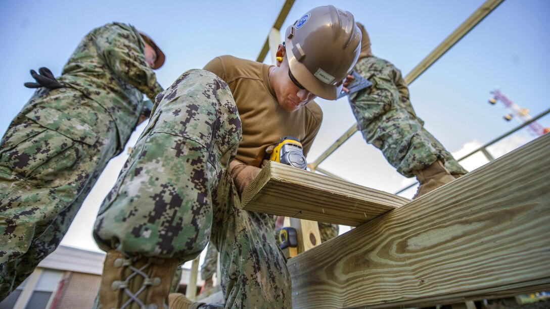 A sailor uses a jigsaw on wood.