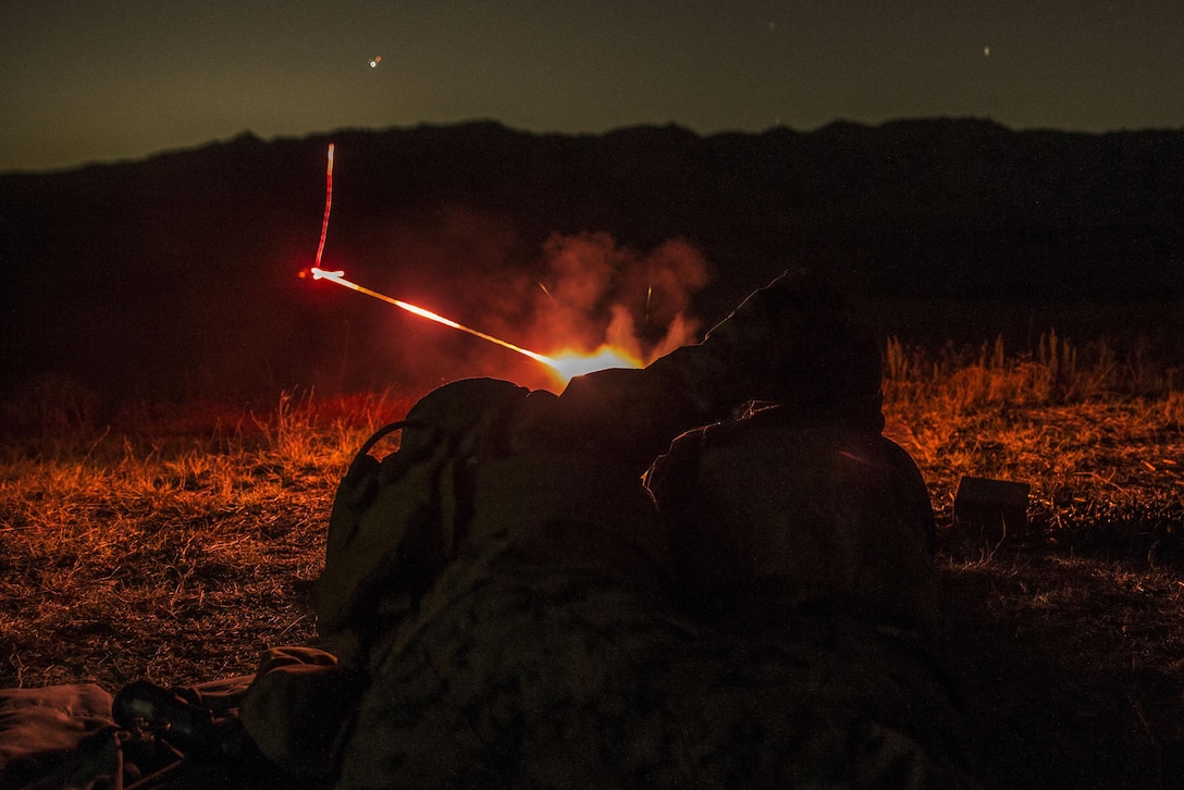 A marine fires a firearm at night.