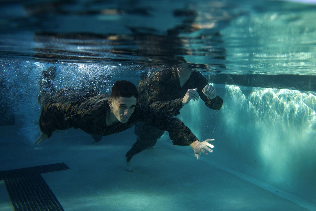 Seen from under water, Marines swim in a pool.
