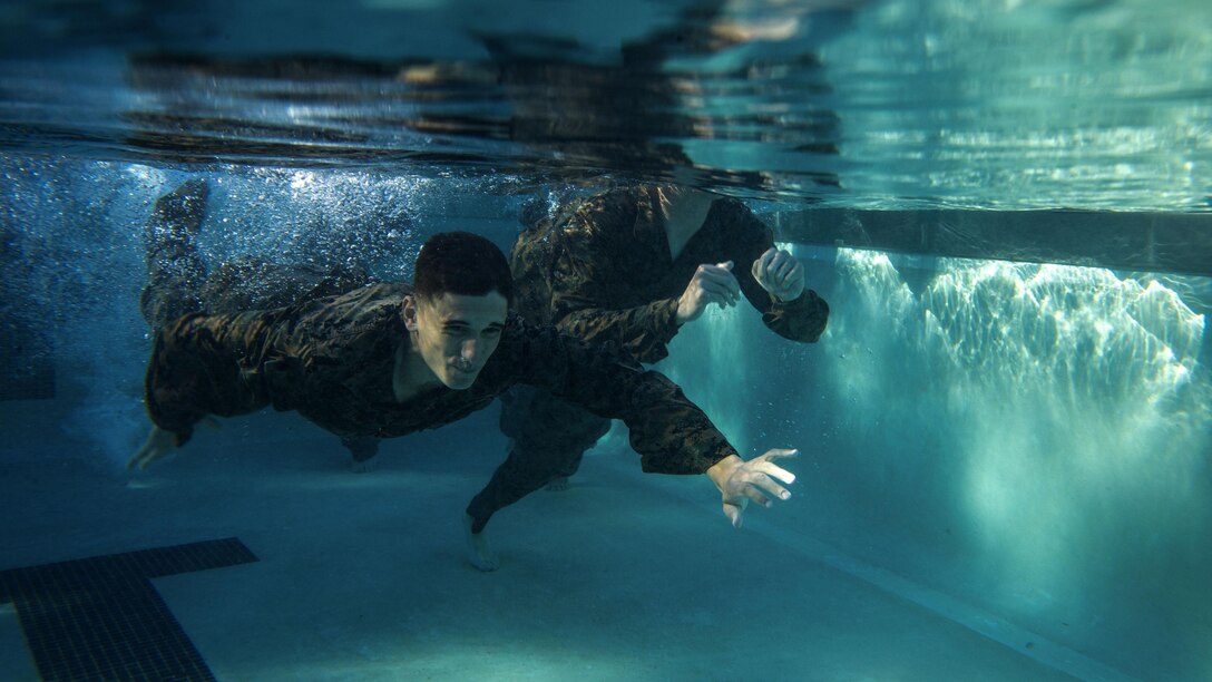 Seen from under water, Marines swim in a pool.