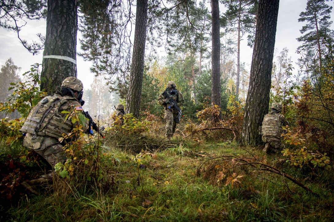 Soldiers move around trees with weapons.