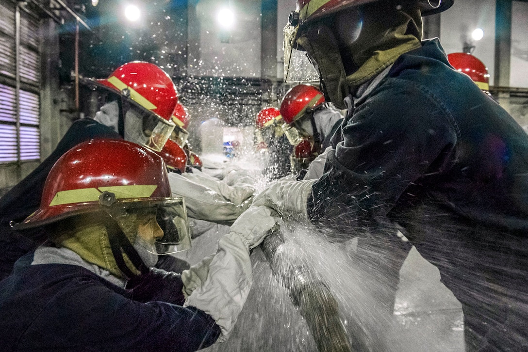 Sailors hold are near a pipe with water spraying.