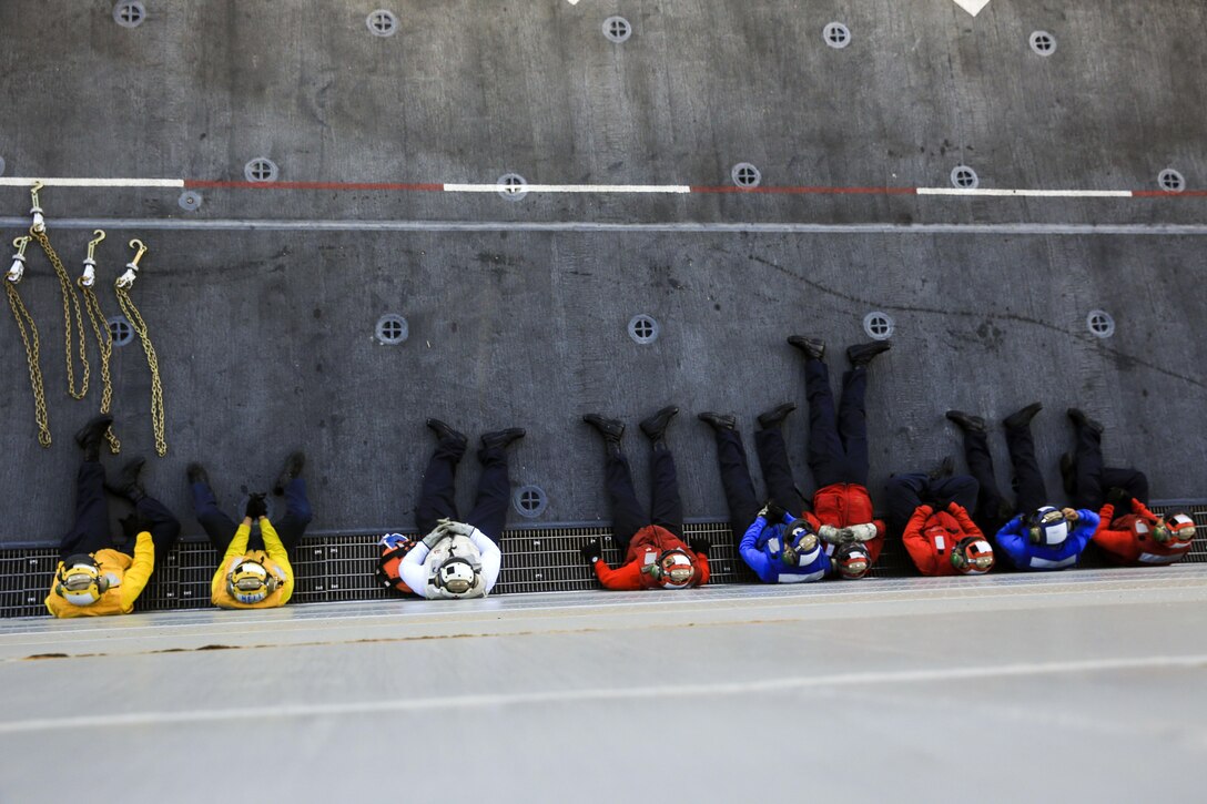 A line of sailors sit against the wall.