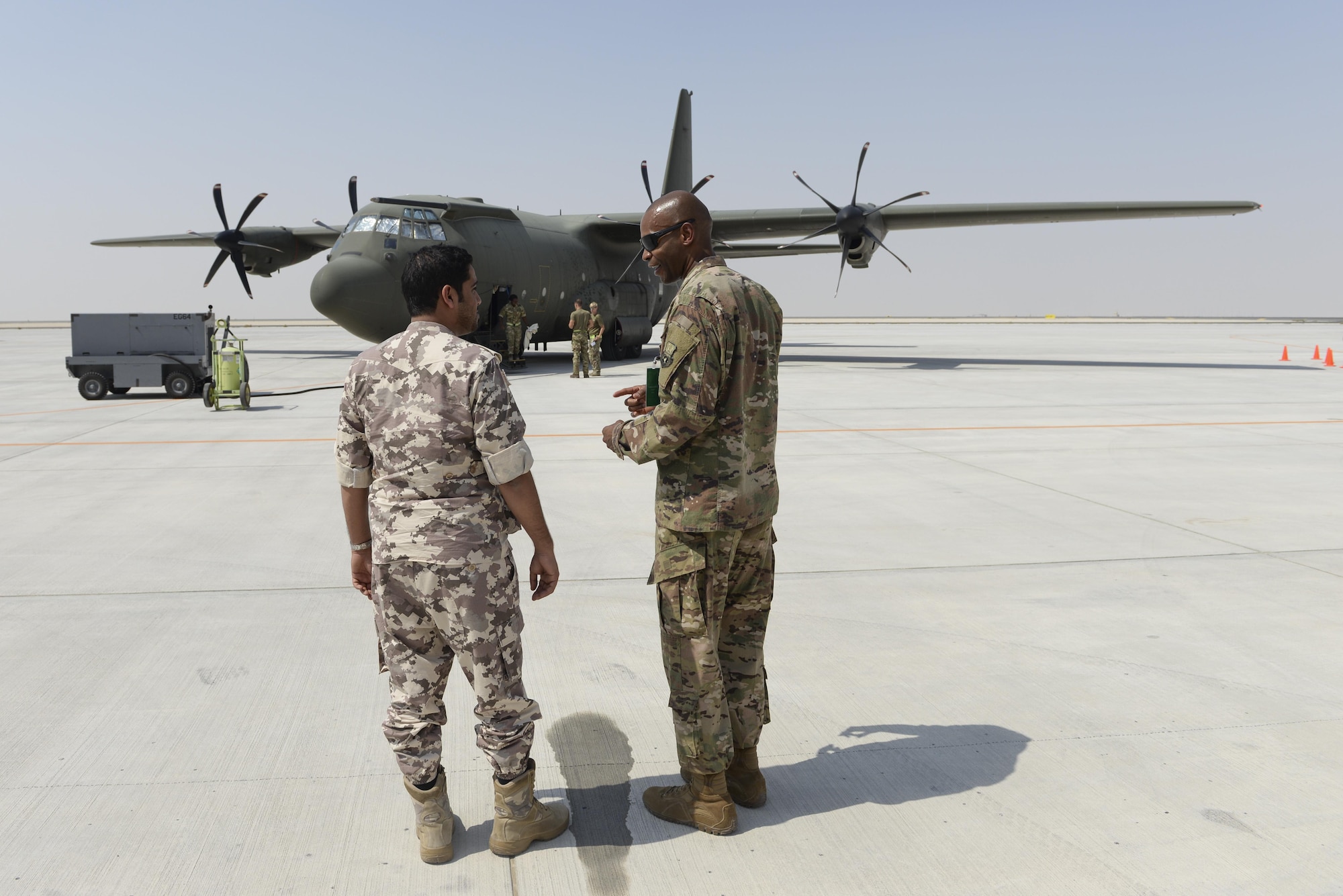 U.S. Air Force Chief Master Sgt. Jerry Williams, command chief assigned to the 379th Air Expeditionary Wing, visits with a member of the Qatar Emiri Air Force as a Royal Air Force C-130J Hercules is off-loaded on the runway at Al Udeid, Air Base, Qatar, Oct. 3, 2017.