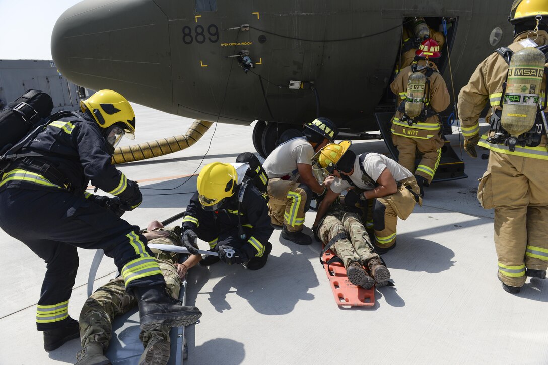 U.S. Air Force firefighters assigned to the 379th Expeditionary Civil Engineering Squadron work alongside firefighters from the Qatar Emiri Air Force, black uniforms, to assist Royal Air Force members, simulating casualties, resulting from the simulated landing gear failure on a C-130J Hercules at Al Udeid Air Base, Qatar, Oct. 3, 2017.