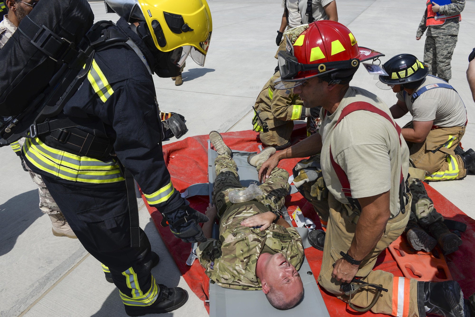 U.S. Air Force firefighters assigned to the 379th Expeditionary Civil Engineering Squadron, tan uniforms, work alongside a firefighter from the Qatar Emiri Air Force, black uniform, to assist Royal Air Force members, simulating casualties, at a staging location at Al Udeid Air Base, Qatar, Oct. 3, 2017.