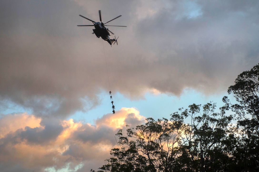 A CH-53E Super Stallion helicopter flies over the treeline during a spy-lining exercise.