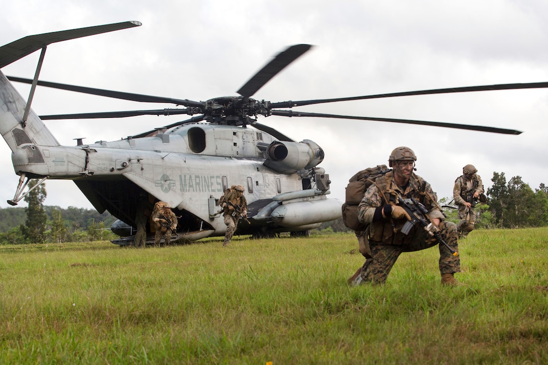 A Marine kneels in front of a helicopter as other troops rush out.