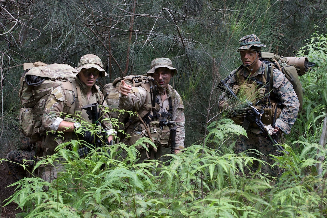 Service members with camouflaged faces stand in a clearing during a jungle patrol.