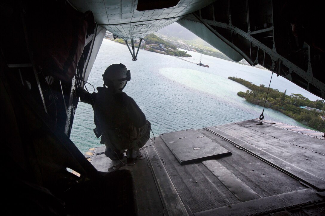 A silhouetted Marine looks out over water from the tailgate of a CH-53 Super Stallion helicopter.