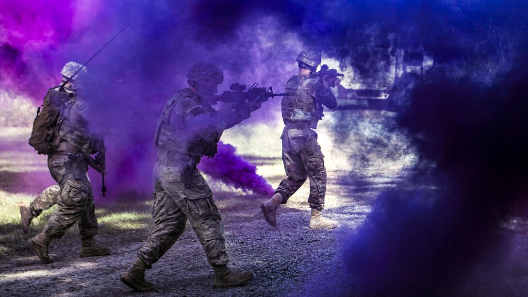 Airmen run through purple smoke.