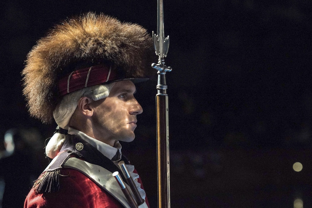 A soldier wearing a white wig and a large fur head covering holds a ceremonial rifle in front of him.