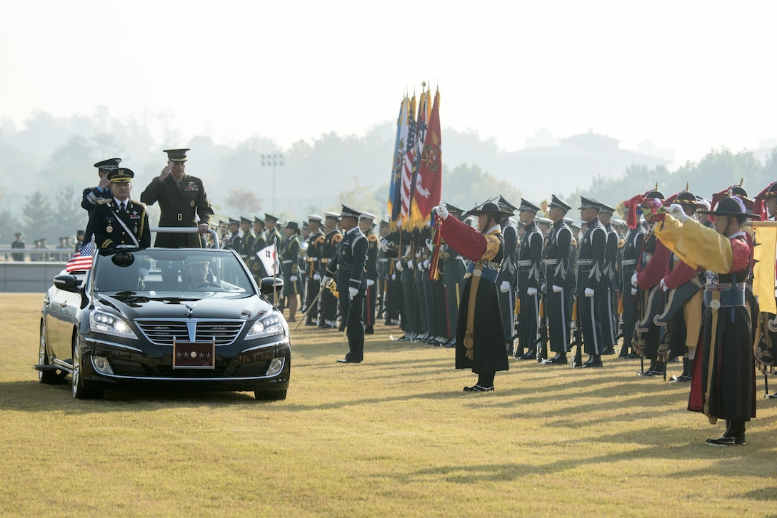 The chairman of the Joint Chiefs of Staff stands in the back of a car while passing South Korean military personnel.