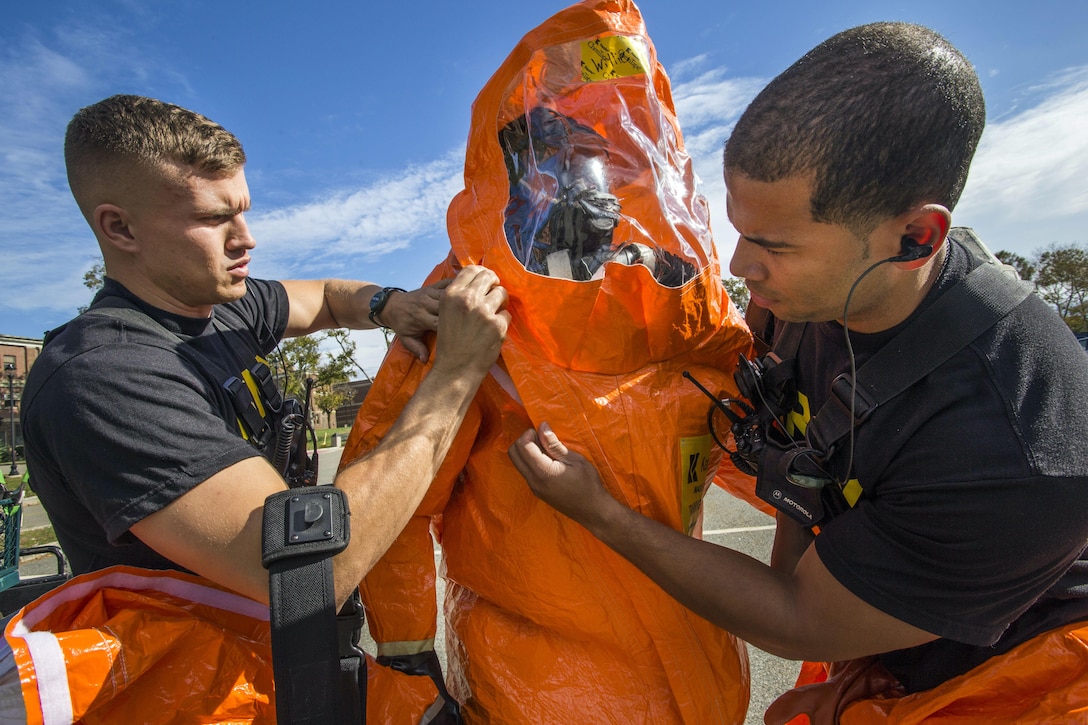 Two soldiers seal a protective suit of a third soldier.