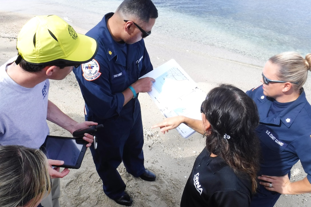 Four people look at paperwork held by a Coast Guardsman.
