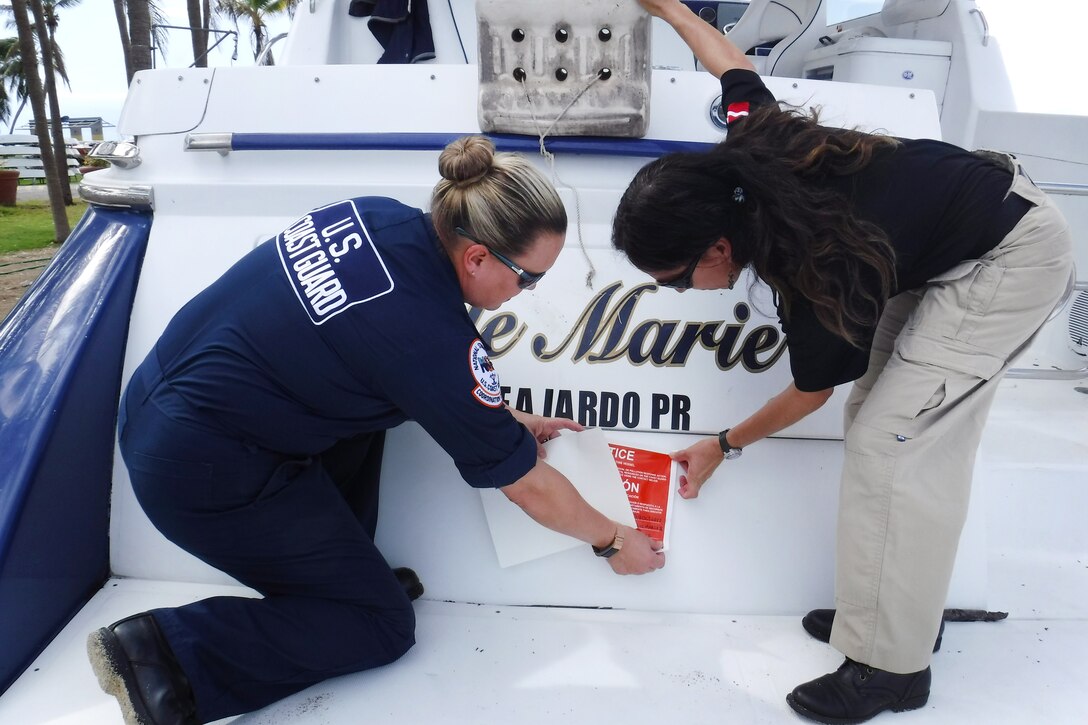 Two people place a large sticker on a boat.