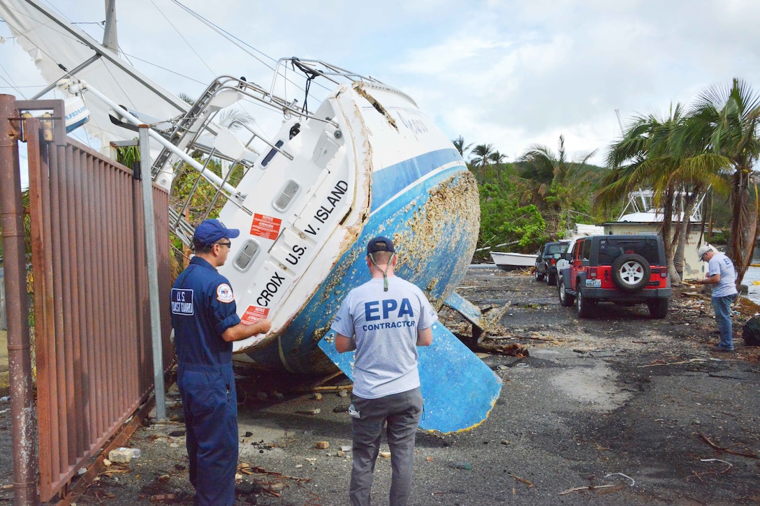 Two people stand next to a boat on dry land.