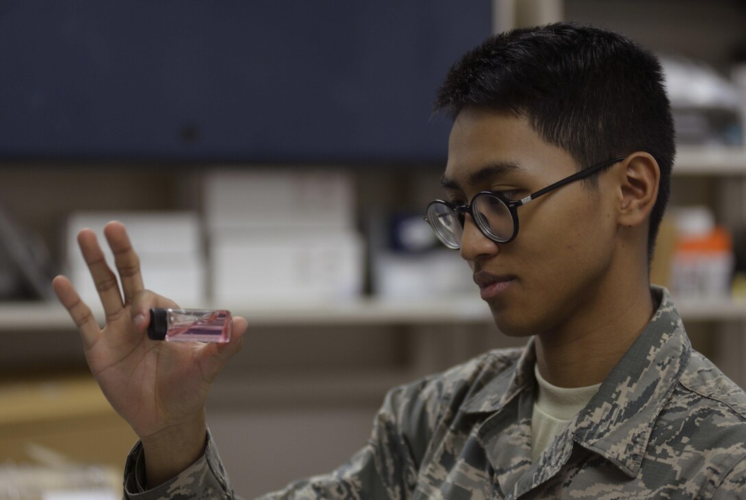 Airman looks at liquid-filled vial.