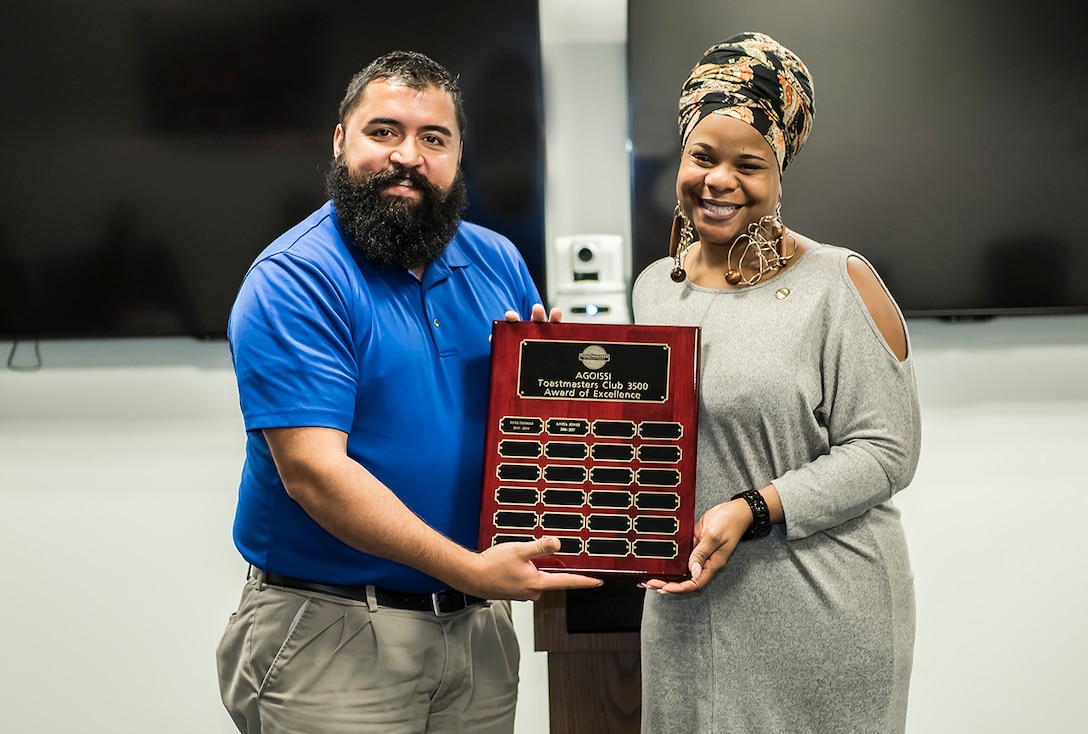 Former DLA Toastmasters AGOISSI Club President Christopher Hancock presents current Club President Anita Jones with the 2017 Frank Chi Award of Excellence.