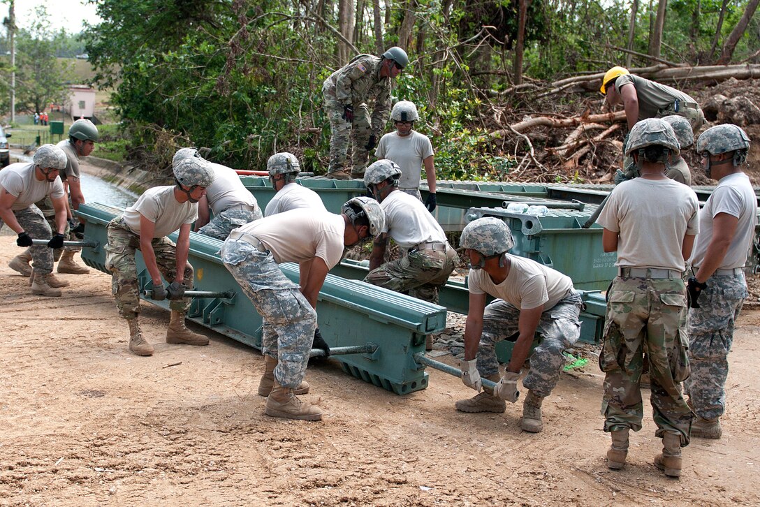 A group of soldiers picks up a piece of bridge.