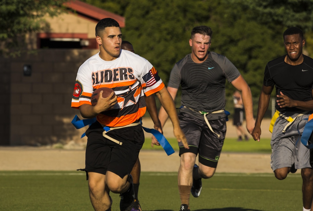 U.S. Marine Corps Cpl. Derycs Miranda (far left), an administrative specialist assigned Headquarters & Headquarters Squadron (H&HS), leaves opposing team members in the turf as he runs toward the end zone in hopes of scoring for his team on Ramada Field at Marine Corps Air Station Yuma, Ariz., Aug. 7, 2017. Later during the game, Miranda scored one touchdown against Marine Aviation Logistics Squadron (MALS) 13, which lead to the H&HS 14-12 victory. (U.S. Marine Corps photo taken by Lance Cpl. Isaac D. Martinez)