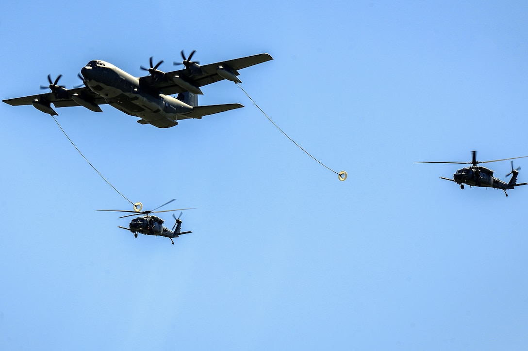 Two HH-60 Pave Hawk helicopters and an HC-130J Combat King aircraft perform aerial refueling.