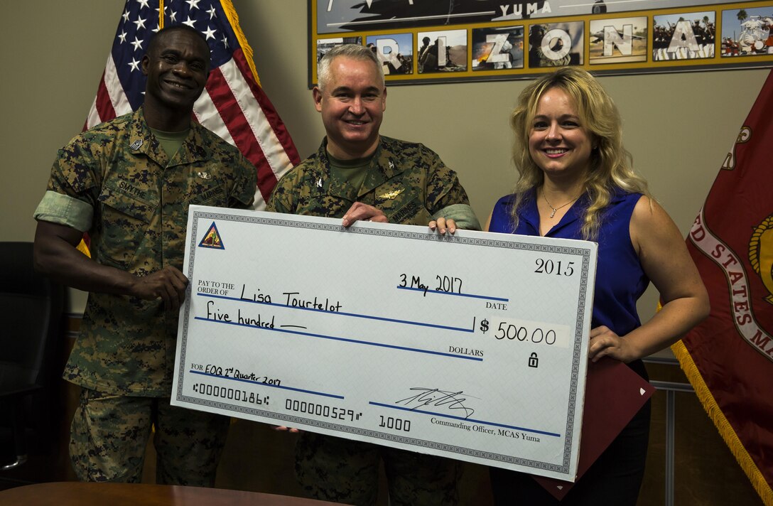U.S. Marine Corps Sgt. Maj. Delvin Smythe (left), the sergeant major of Marine Corps Air Station Yuma, Ariz., and Col. Ricardo Martinez (center), the commanding officer of MCAS Yuma, present Lisa Tourtelot (right), the public affairs assistant for MCAS Yuma Public Affairs and Combat Camera, with a check for five hundred dollars in addition to the MCAS Yuma Employee of the 2nd Quarter award at the station headquarters, May 3, 2017. (U.S. Marine Corps photo taken by Lance Cpl. Christian Cachola)