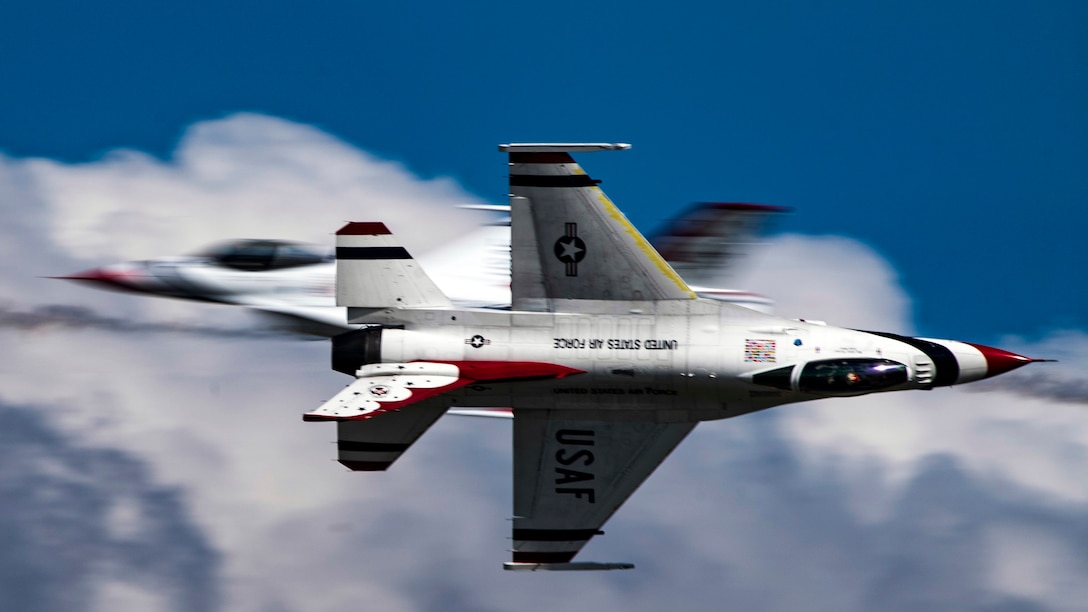 Two fighter jets cross in the sky, one flying straight ahead and the other on its side.