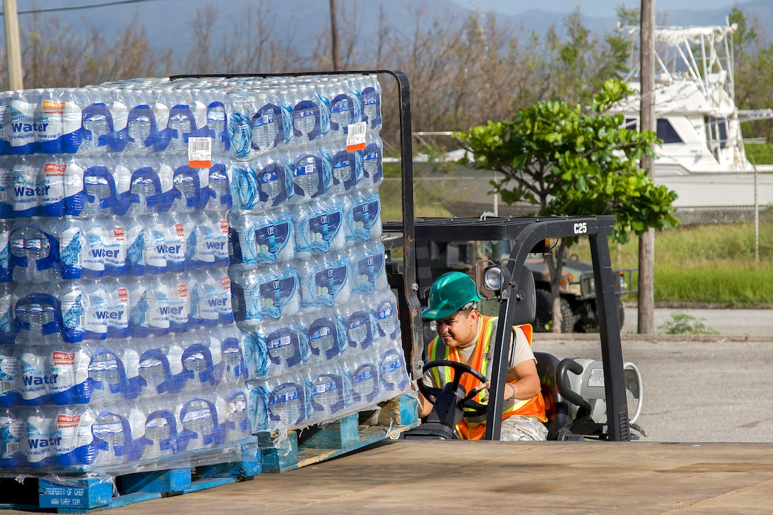 A person using a forklift to lift a pallet of water bottles.