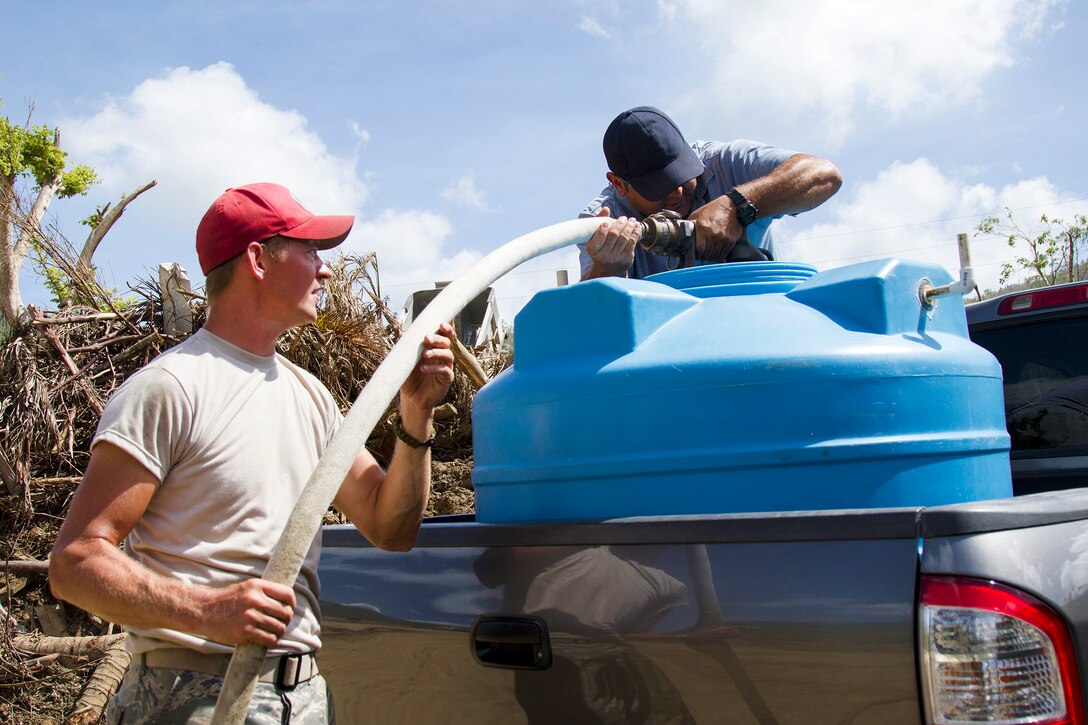 A soldier uses a hose to fill up a water tank in the back of a truck.