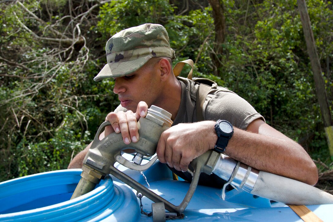 A soldier uses a hose to fill a water tank.