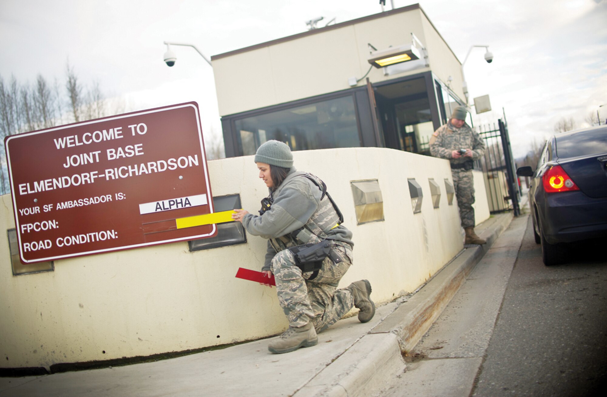 Senior Airman Alessia Figueroa, a patrolman assigned to 673d Security Forces Squadron, left, changes the road condition sign at the Post Road gate as Pfc. Jesse Sherrard, a patrolman assigned to 164th Military Police Company, performs an identification card check on Joint Base Elmendorf-Richardson, Alaska, Oct. 30, 2013. (U.S. Air Force photo by Justin Connaher/Released)