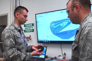 Two men talk in front of a computer screen.