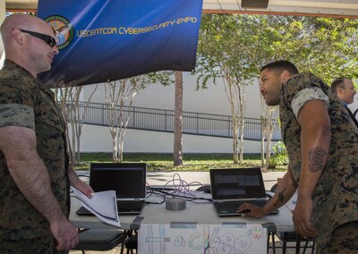 U.S. Marine Corps SSgt Michael George, USCENTCOM cybersecurity technician (Left), and U.S. Marine Corps SSgt. William Berotte, USCENTCOM cybersecurity technician (Right), demonstrate how simple it is to "hack" on older computer operating system at the USCENTCOM cybersecurity awareness expo, October 26, 2017. The expo provided the opportunity for personnel and family members to talk with subject matter experts and view exhibits that highlight best security practices, in the workplace and home, to protect critical and personal information online.