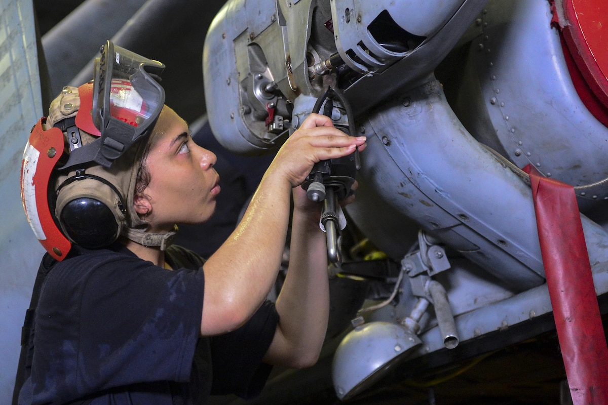 A sailor maintains a crane for a Seahawk helicopter.