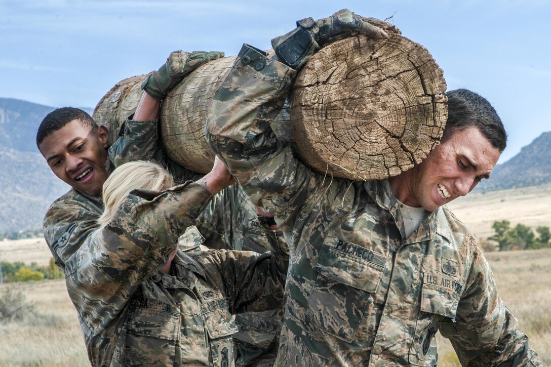 Three airman carry a log on their shoulders.