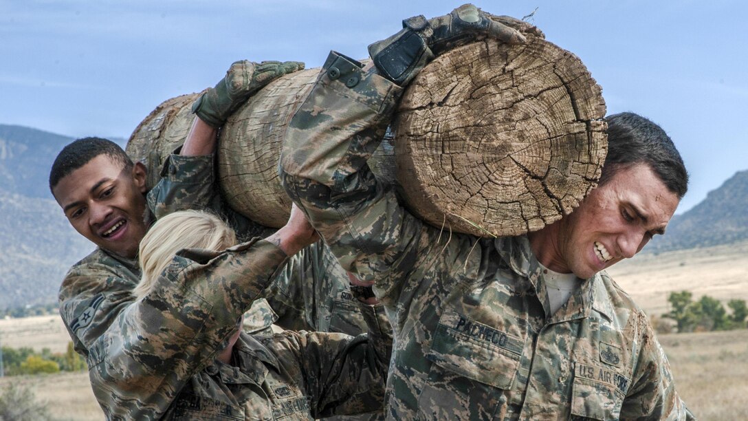 Three airman carry a log on their shoulders.