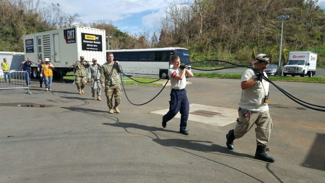 Soldiers from the 249th Engineer Battalion and contractors carry cabling to support a generator. The team is installing the generators around Puerto Rico to support critical facilities like hospitals and emergency services.