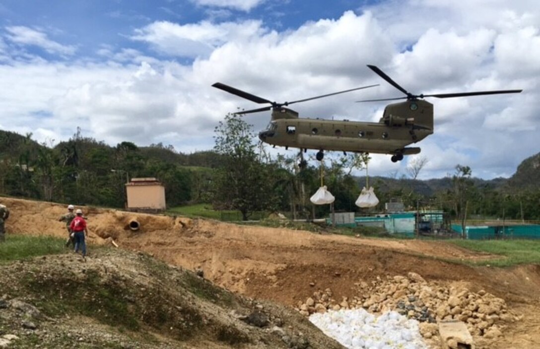 A Chinook helicopter from the Georgia National Guard places 3,000-pound supersacks in the damaged spillway. Altogether, 505 jersey barriers and 1,300 supersacks will be placed to minimize further erosion in the damaged spillway.