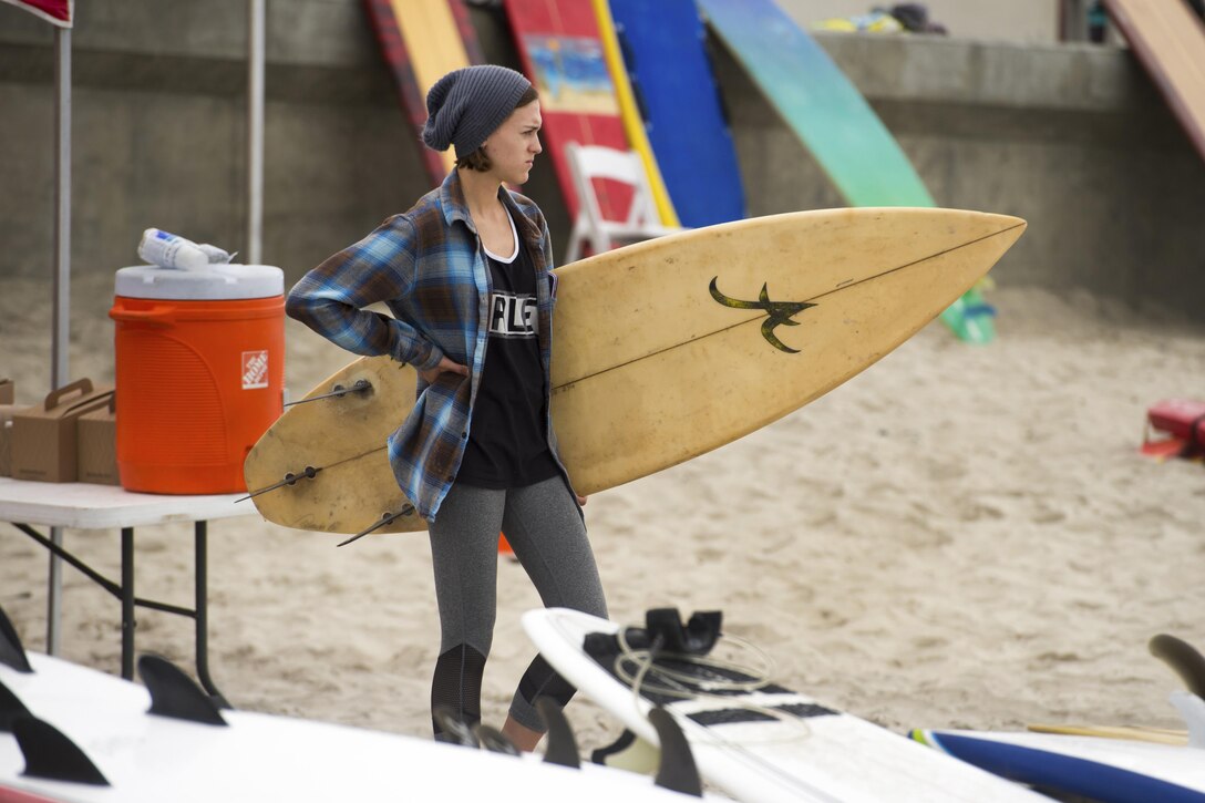 A surfer stands holding a surf board.