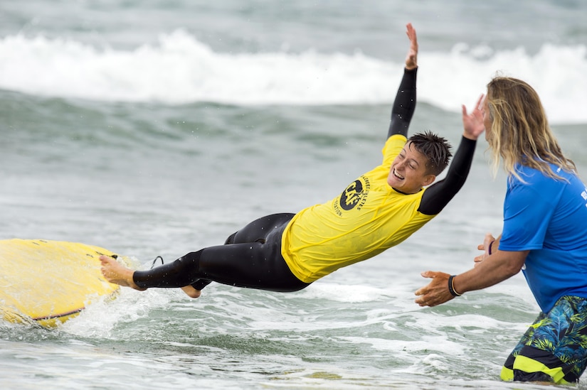 A surfer free falls from a surfboard and next to an instructor.